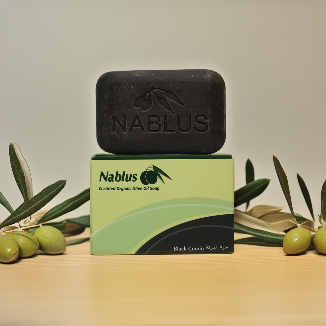 Black cumin and olive oil soap bar standing up on a wooden table with olive branches and green olives around it