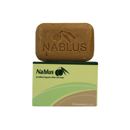 cinnamon and olive oil soap bar made by nablus soap company, the soap bar is standing on top of its packaging reading nablus certified organic olive oil soap and the blend name nablus the soap bar is a toasted brown color with flecks of cinnamon in it