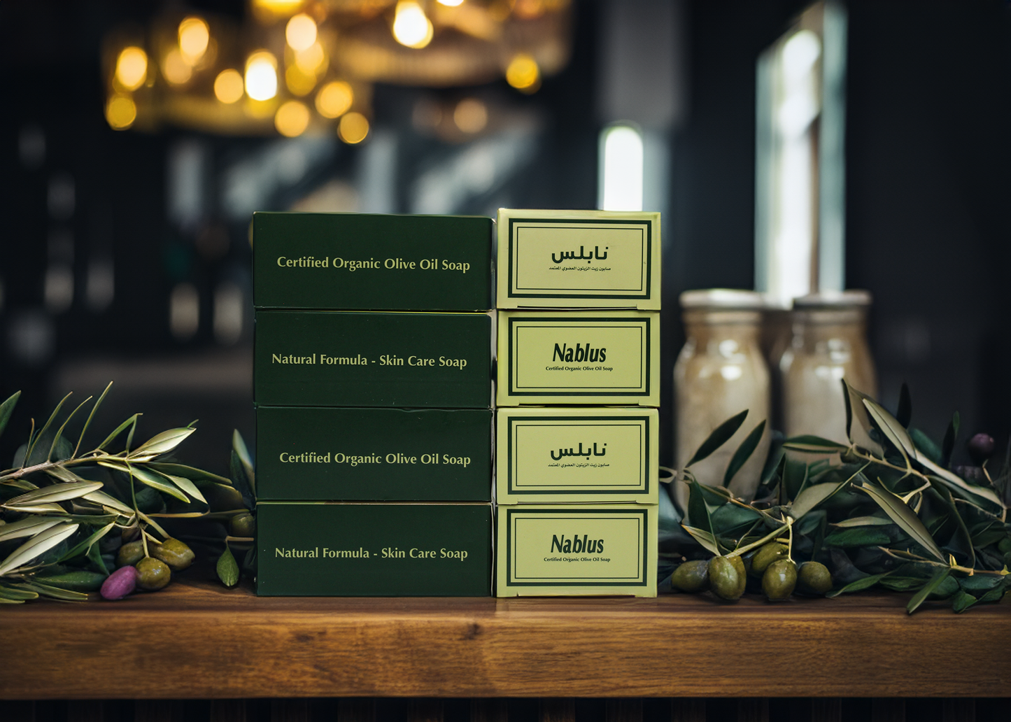 Stacked boxes of nablus soap companys soap bars, showcasing the green packaging and words reading Nablus Certified Organic Olive Oil soap Natural Formula Skin Care Soap with olive branches around it and olives