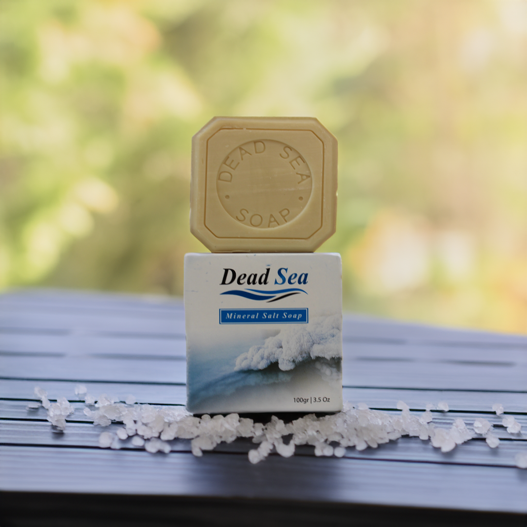 dead sea salt and olive oil soap on a wooden table with greenery in the background with dead sea salt around it